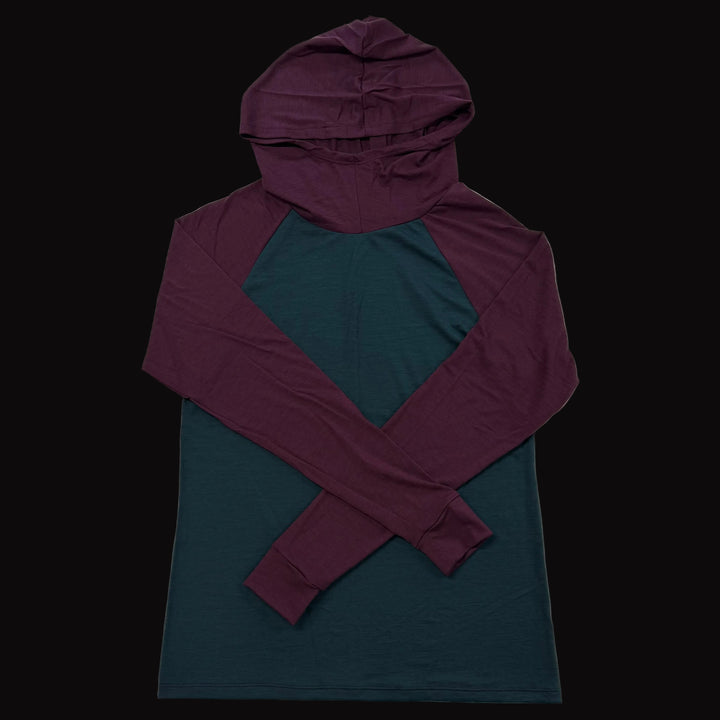A long-sleeve hooded shirt laid flat on a light gray background, featuring a dark teal body and a contrasting deep purple hood and sleeves.